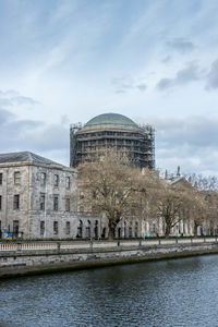 View of building by river against cloudy sky