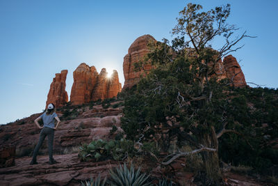 Man on rock by trees against clear sky