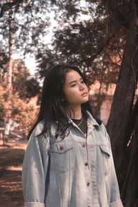 Thoughtful young woman standing against trees at park