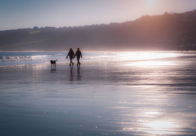 Silhouette people on beach against sky during sunset