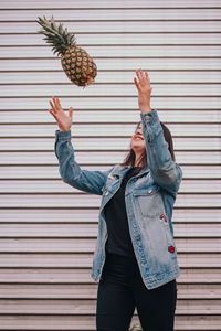 Woman playing with pineapple while standing against wall