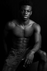 Portrait of young man sitting against black background