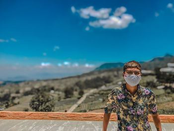 Portrait of young man wearing mask standing against blue sky