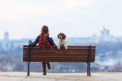 Full length of woman with dog sitting on bench against sky