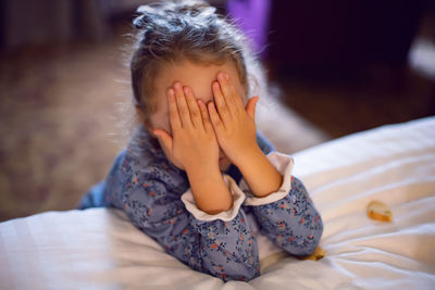 Five year old girl child covered her eyes with her hands near the bed in the hotel