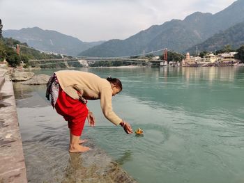 Full length of woman standing by river against mountains