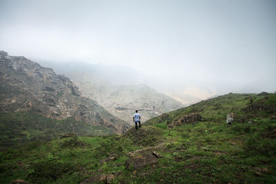 Rear view of man standing on mountain against sky