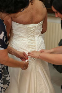 Midsection of women helping bride to get dressed