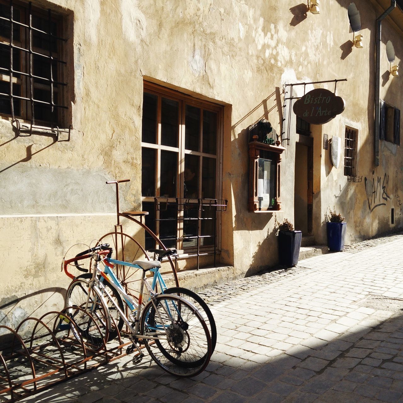 bicycle, architecture, building exterior, built structure, parking, parked, stationary, land vehicle, transportation, house, mode of transport, window, residential structure, residential building, building, wall - building feature, street, sunlight, cobblestone, wall