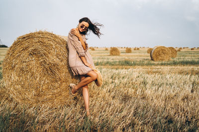 Smiling woman in sunglasses with bare shoulders on a background of wheat field and bales of hay.