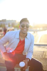 Portrait of young man wearing sunglasses while sitting on railing
