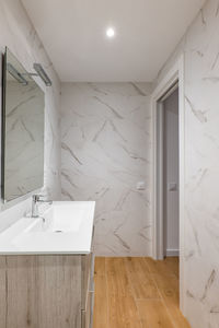 Bathroom with white tiles, mirror, ceramic sink under a wardrobe in a modern house or office.