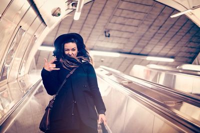Portrait of young woman gesturing while standing on escalator illuminated subway station