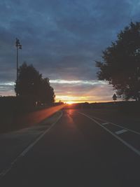 Road by silhouette trees against sky at sunset