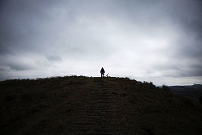 People walking on landscape against cloudy sky