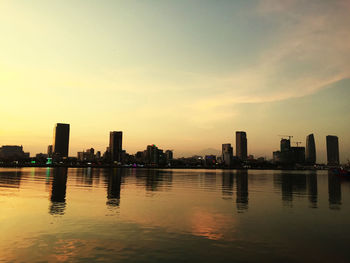 Scenic view of river by buildings against sky during sunset