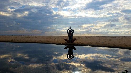 Full length of woman doing yoga in lotus position at beach against sky