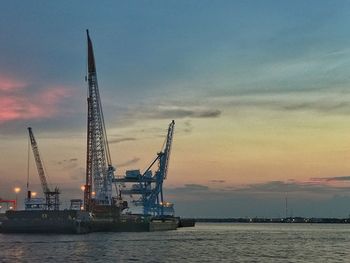 Cranes by sea against sky during sunset