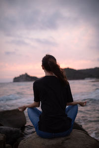 Rear view of woman doing yoga on rock at beach during sunrise