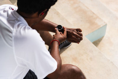 High angle view of man holding wristwatch sitting outdoors