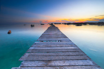 Damaged pier at sea against sky during sunset