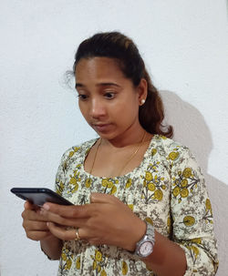 Portrait of young woman using phone while standing against wall