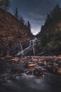 Stream flowing through rocks in forest against sky