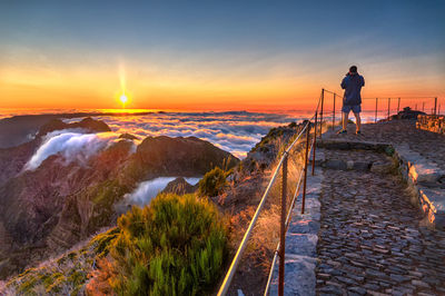 Man standing on shore against sky during sunset