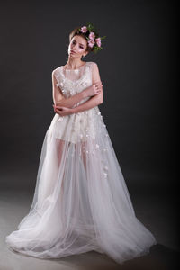 Portrait of young woman in wedding dress standing against black background