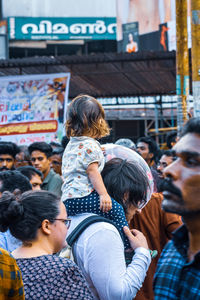 Rear view of friends standing against people in city