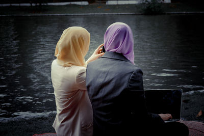 Rear view of women sitting by lake