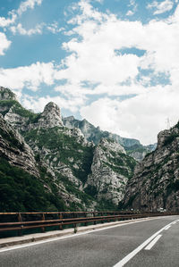 Road leading towards mountains against cloudy sky