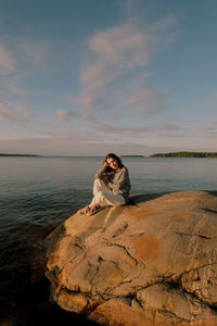 Woman sitting on rock by sea against sky