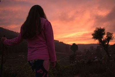 Rear view of woman standing against sky during sunset