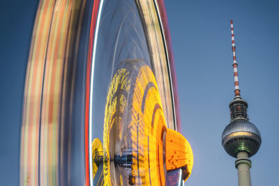 Low angle view of spinning ferris wheel by fernsehturm tower against sky