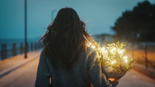 Young girl walks with a bouquet of plants and party lights in her hand