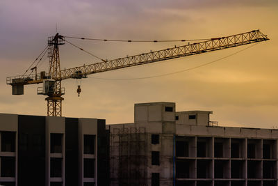 Low angle view of crane at construction site against sky during sunset