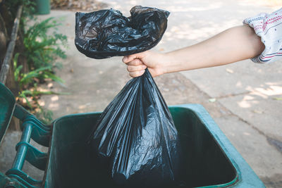 Cropped hand of woman putting plastic bag in dustbin