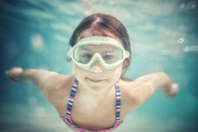 Girl wearing goggles swimming towards camera underwater