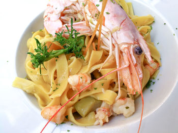 High angle view of tagliatelle and prawns garnished with cilantro served in bowl on table