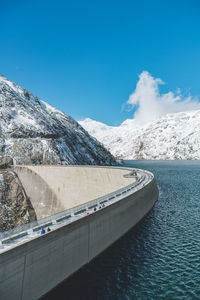 Scenic view of river by snowcapped mountains against blue sky