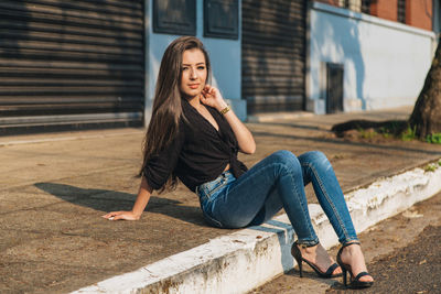 Portrait of young woman sitting on footpath in city