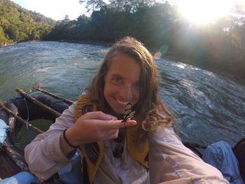 Portrait of smiling young woman holding river against trees