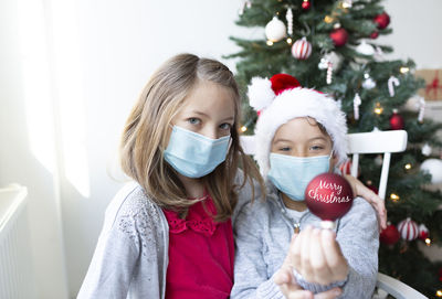 Portrait of siblings wearing mask against christmas tree at home