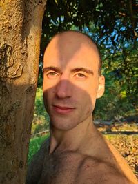 Portrait of smiling young man against tree trunk