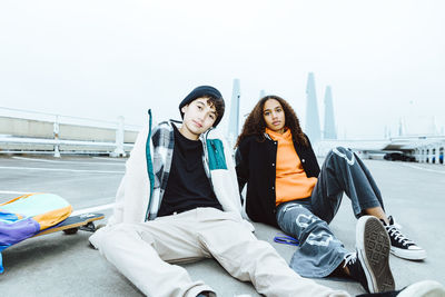 Portrait of male and female friends sitting on street against clear sky