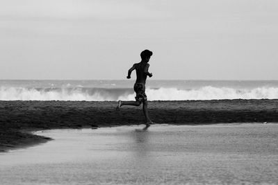 Side view of shirtless man on beach against sky