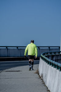Rear view of man walking on bridge against clear sky