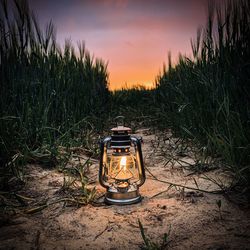 Illuminated lantern on field against sky during sunset