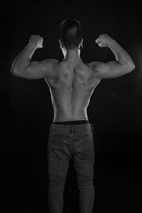 Rear view of shirtless man standing against black background